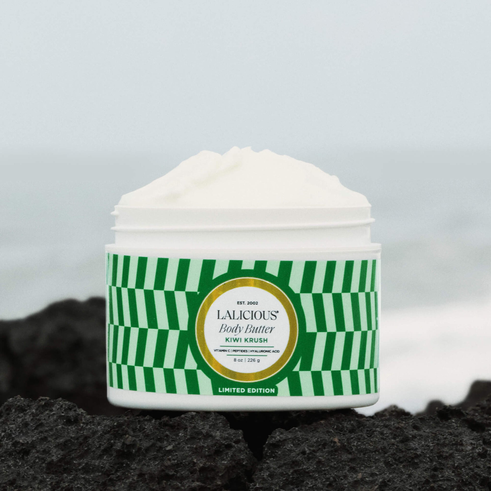 8oz Kiwi Krush Body Butter jar without a cap sitting on a rock in the beach- LALICIOUS