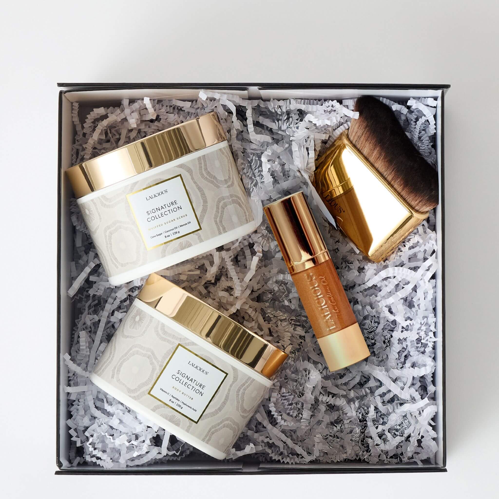 The Signature Spa Collection - Top shot of a box with crinkle paper and Body Butter, Body Scrub, Golden Oil and Body Brush. LALICIOUS